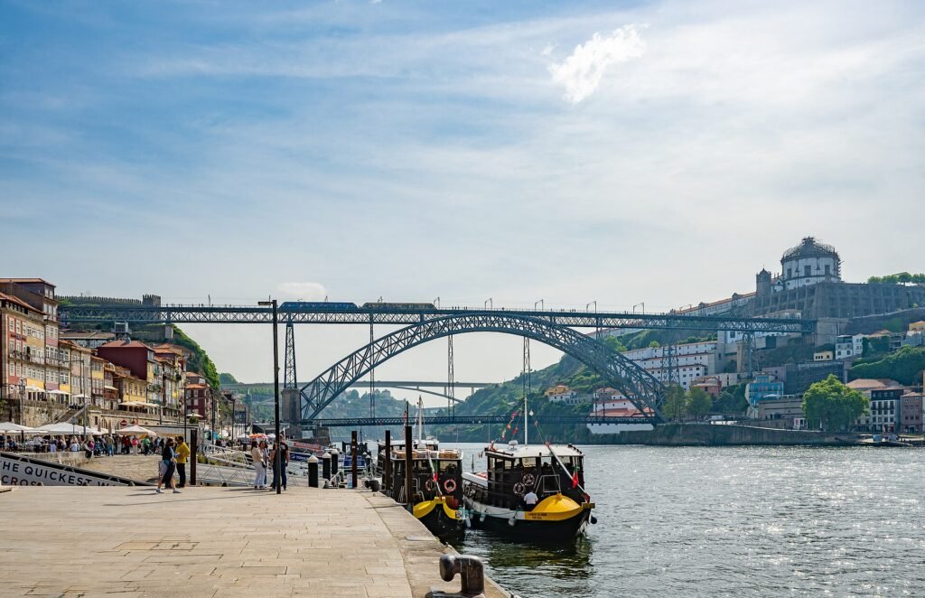 This vibrant photograph captures the majestic Dom Luís I Bridge in Porto, Portugal, spanning the glittering Douro River. On the left bank, c