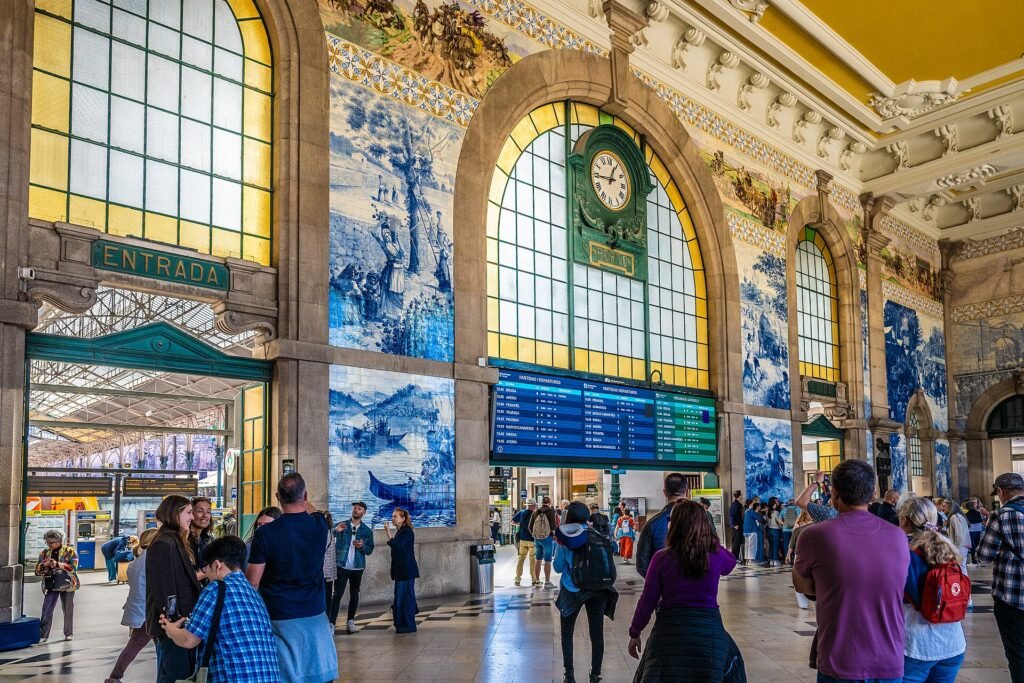 The photograph captures the magnificent interior of Porto's São Bento train station, renowned for its stunning azulejo tile panels. Large ar